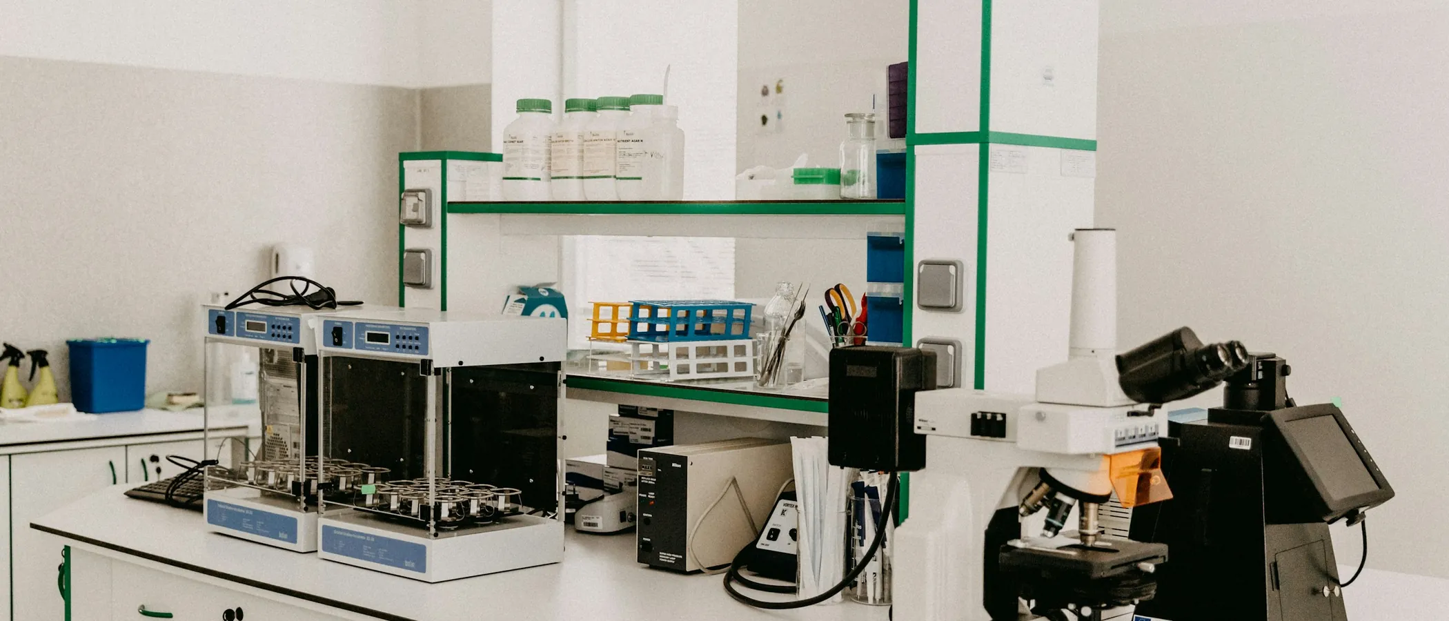 A laboratory bench in a bright room: analytical instruments along it, a microscope at the near end.