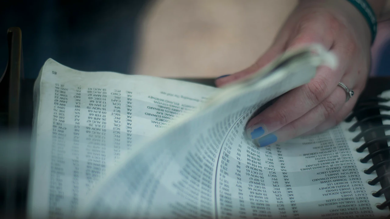 The printed paper open on a table, hands turning a page.