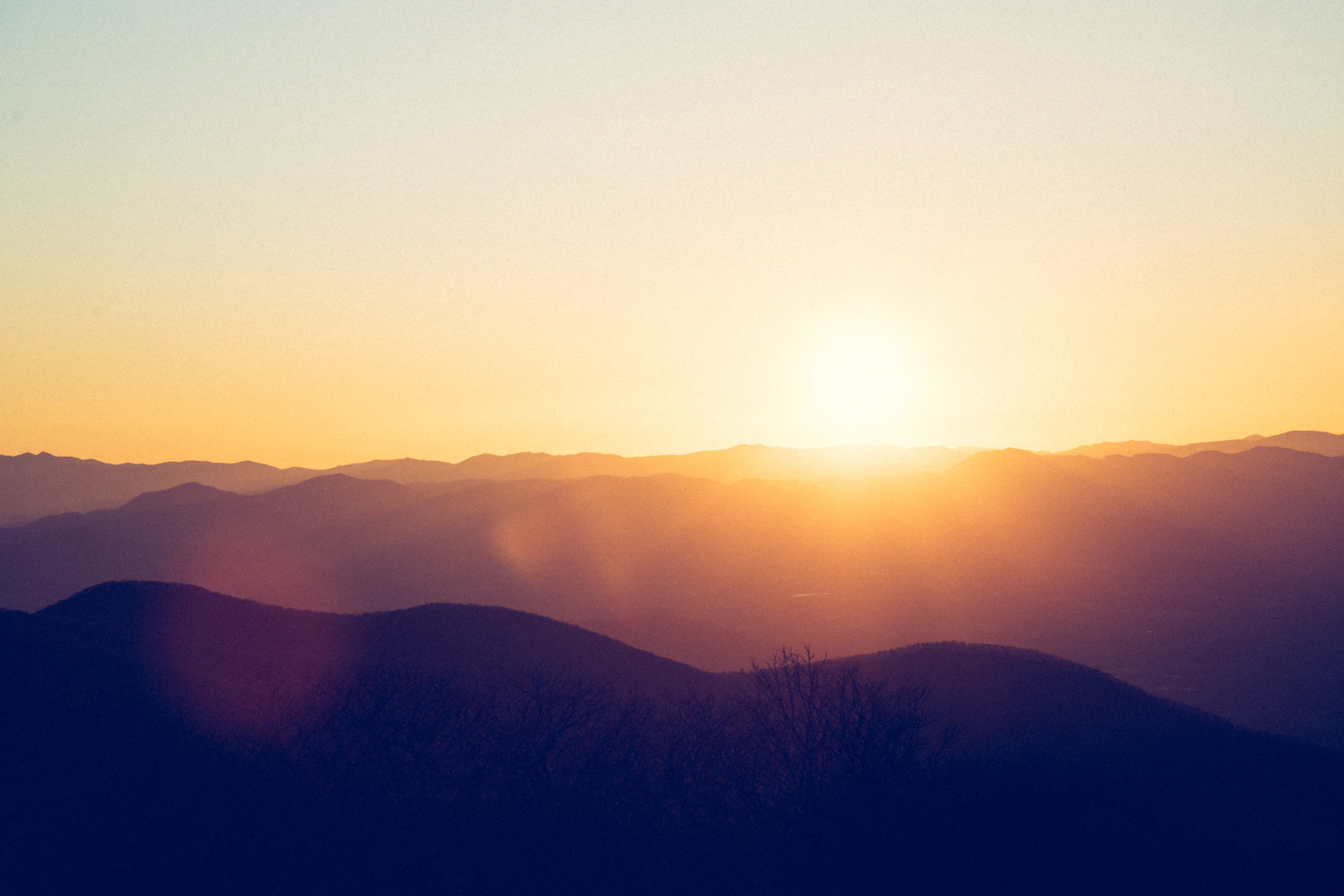 The sun setting behind layered mountain ridges in a warm haze.
