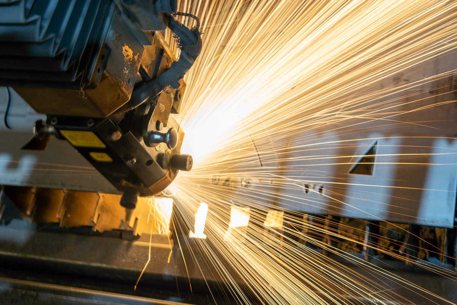 A laser cutting head throwing a fan of sparks across a metal sheet.