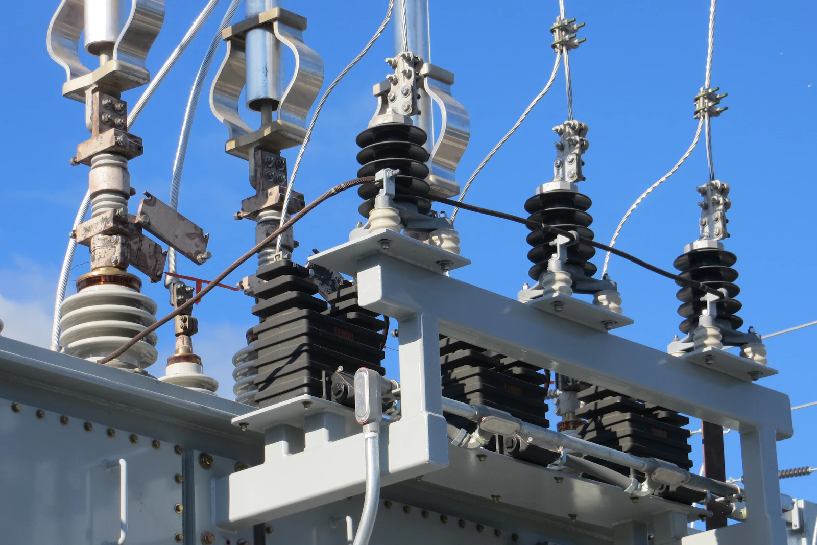 Insulators and bus bars on an electrical substation against a blue sky.