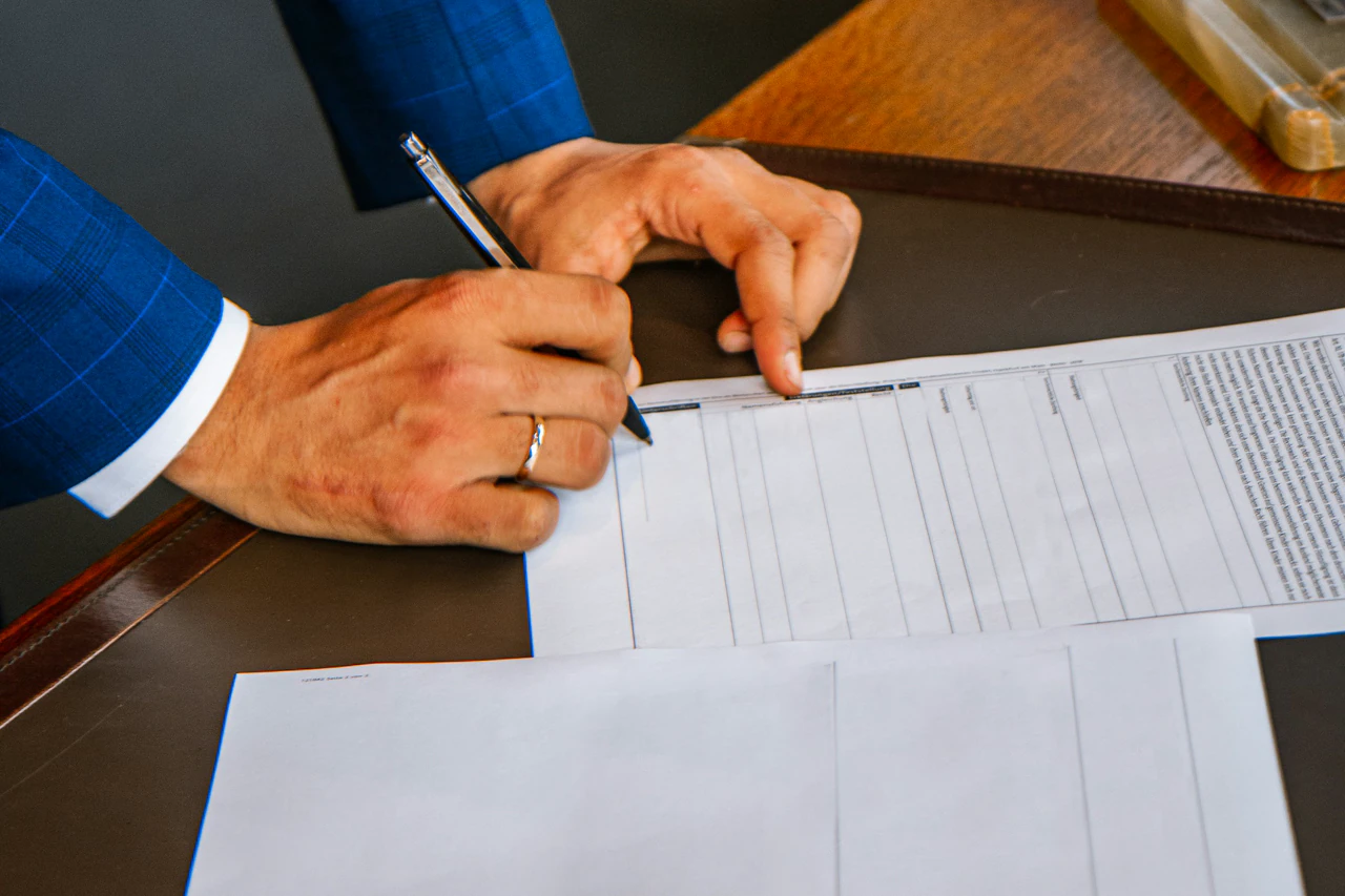 A renewal form signed at a desk, pen in hand, papers squared beside it.